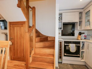 Eine Holztreppe führt zu einer Küche mit weißen Schränken, einem Herd und einer Mikrowelle.