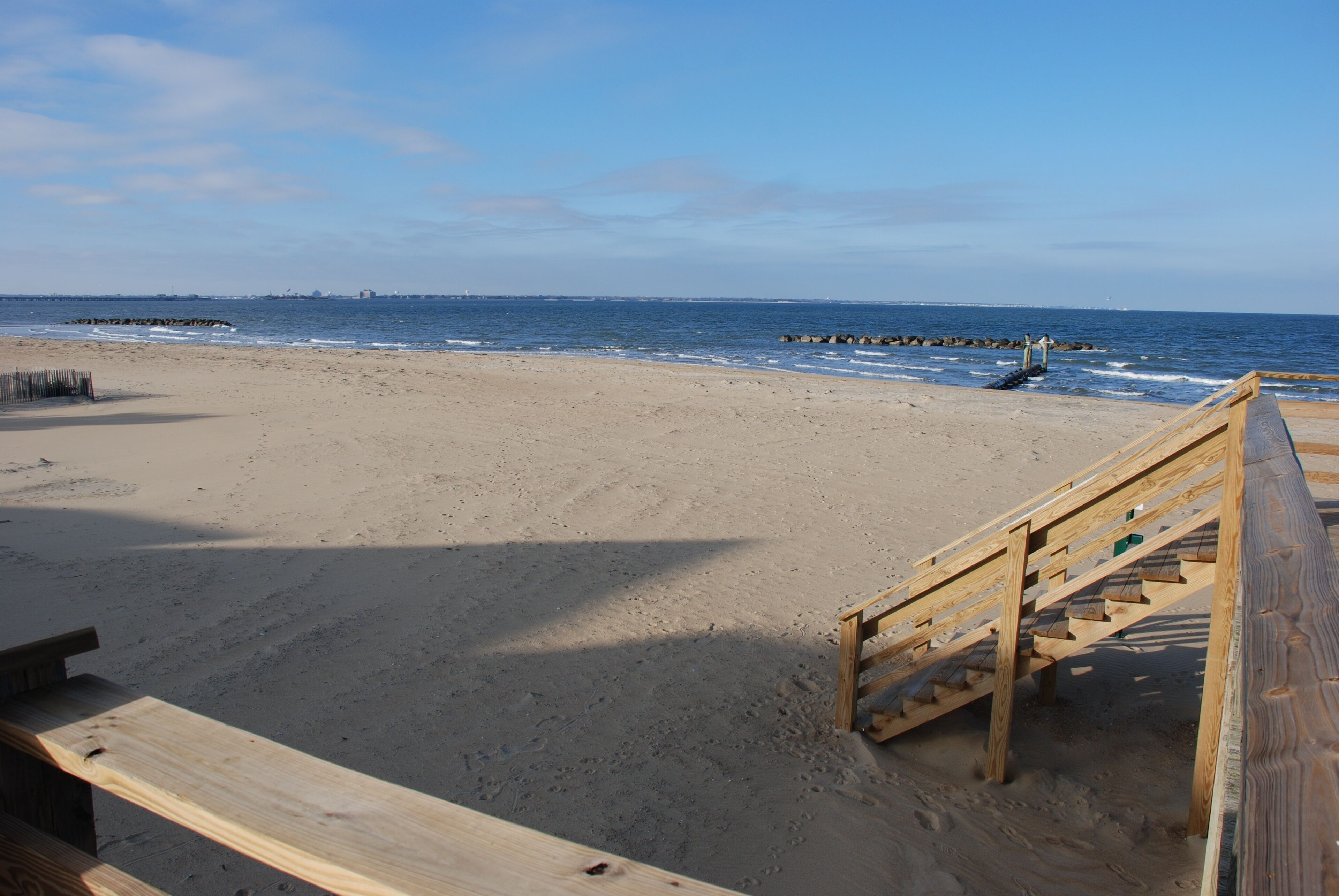 A wooden staircase leading to a sandy beach with a clear sky.