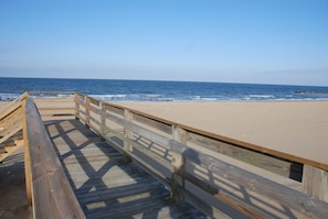 A wooden boardwalk leading to a sandy beach with the ocean in the background.