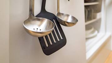 A kitchen with a white wall, a black spatula, and a stainless steel ladle hanging on the wall.