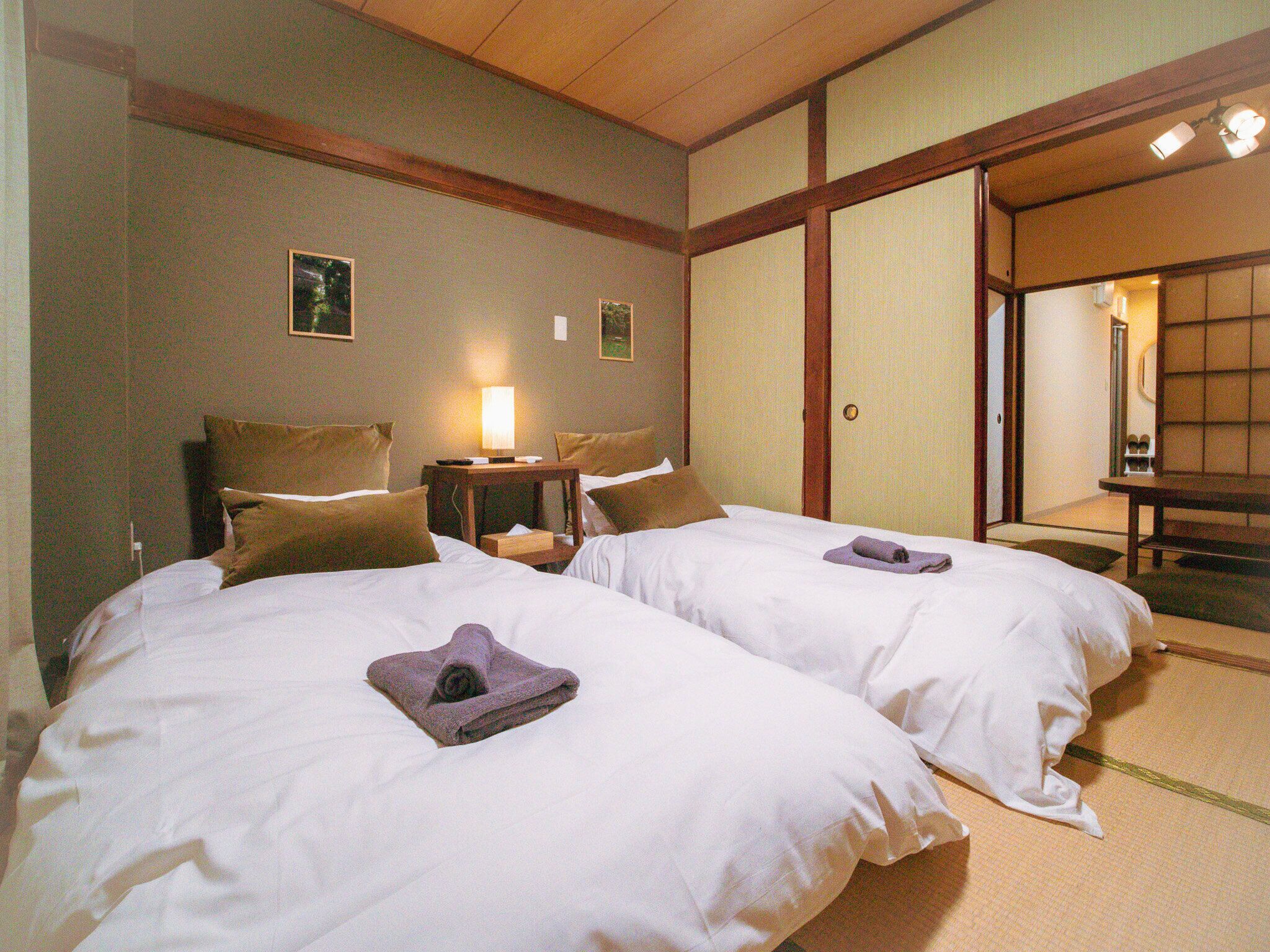 A hotel room with two beds, a bedside table with a lamp, and a traditional sliding door.