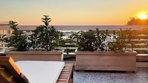 Una terraza en la azotea con vistas a la puesta de sol, sillones de madera para relajarse y plantas en macetas.