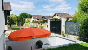 Un quartier résidentiel avec une maison blanche, un portail noir et un parapluie rouge.