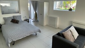 Une chambre à coucher comprenant un lit, un canapé, une fenêtre donnant sur un espace verdoyant, un radiateur et un luminaire au plafond.