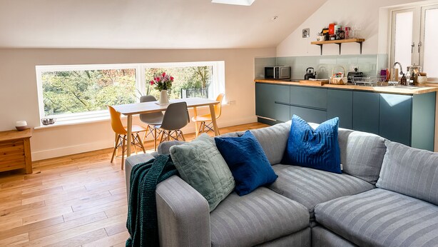 Un appartement moderne de style « loft », comprenant un coin repas, une cuisine et un espace de vie confortable avec un canapé et une grande fenêtre.