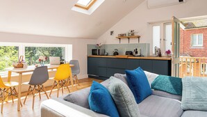 Une cuisine moderne dotée d’une verrière, un coin repas avec des chaises jaunes et un espace de vie chaleureux avec un canapé et des coussins.