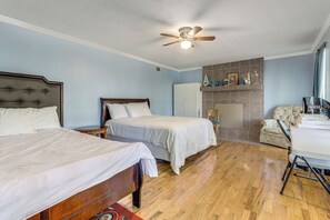 A bedroom with two beds, a ceiling fan, a fireplace, and a desk.