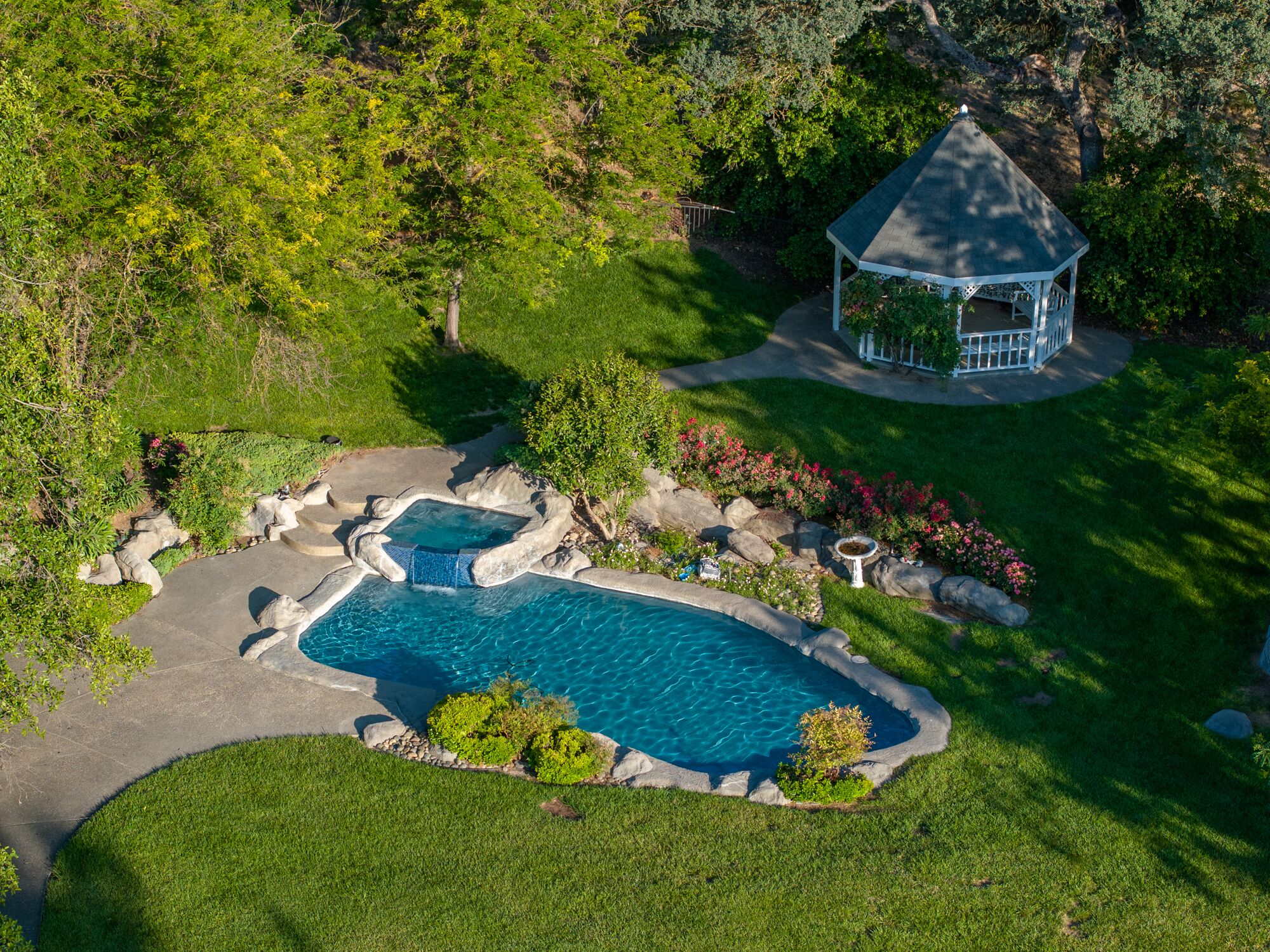 A swimming pool with a hot tub, surrounded by a landscaped garden with a gazebo.