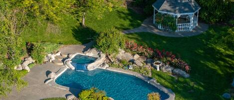 A swimming pool with a hot tub, surrounded by a landscaped garden with a gazebo.