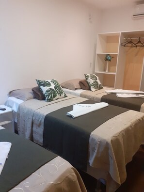 A hotel room with two beds, each with a pillow and a blanket. There is a shelf with a plant and a hanging coat rack.