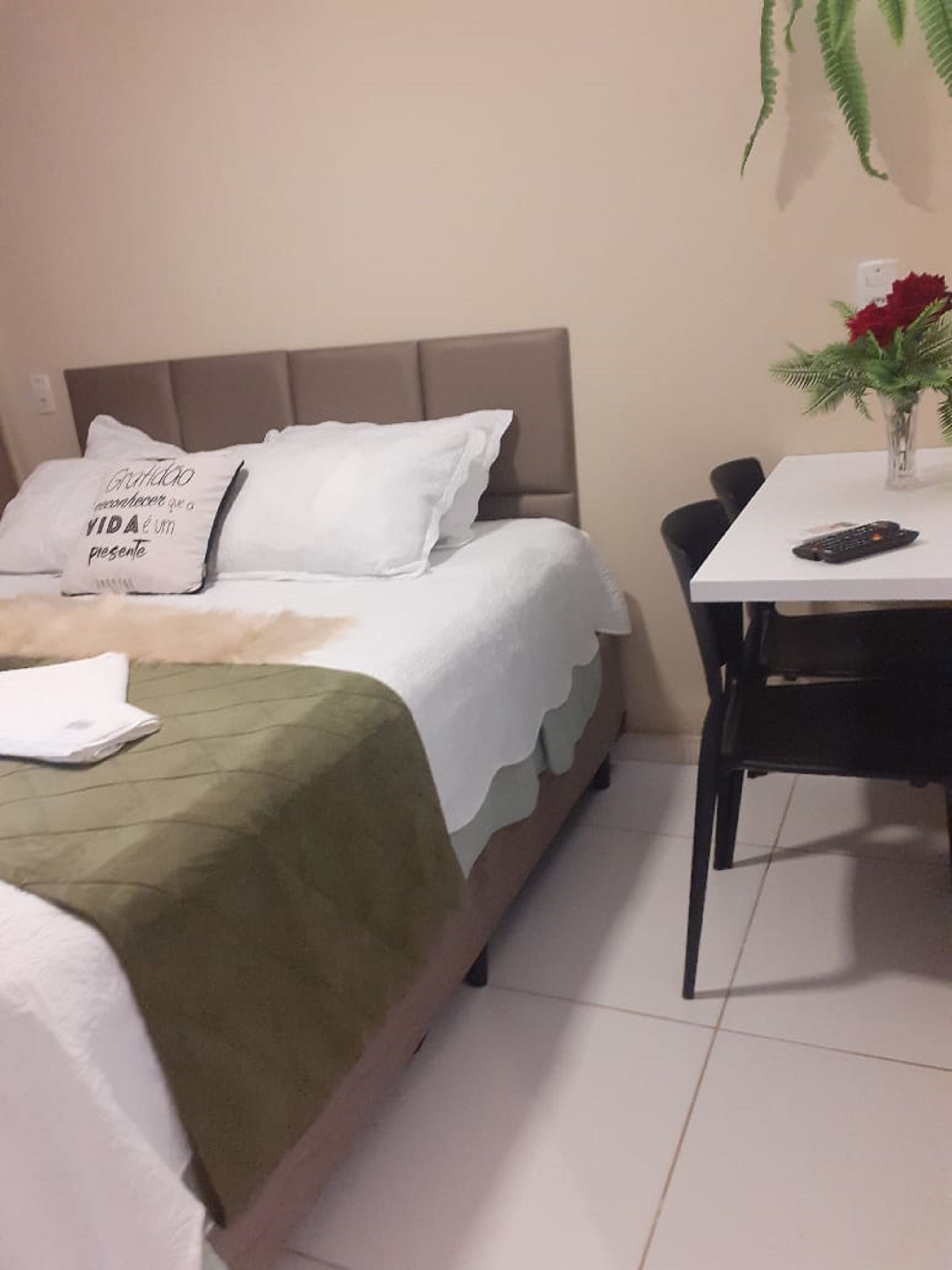Een keurig opgemaakte slaapkamer met een bed, een tafeltje met een bloevas en een stoel.