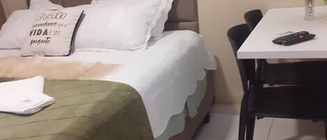 Een keurig opgemaakte slaapkamer met een bed, een tafeltje met een bloevas en een stoel.
