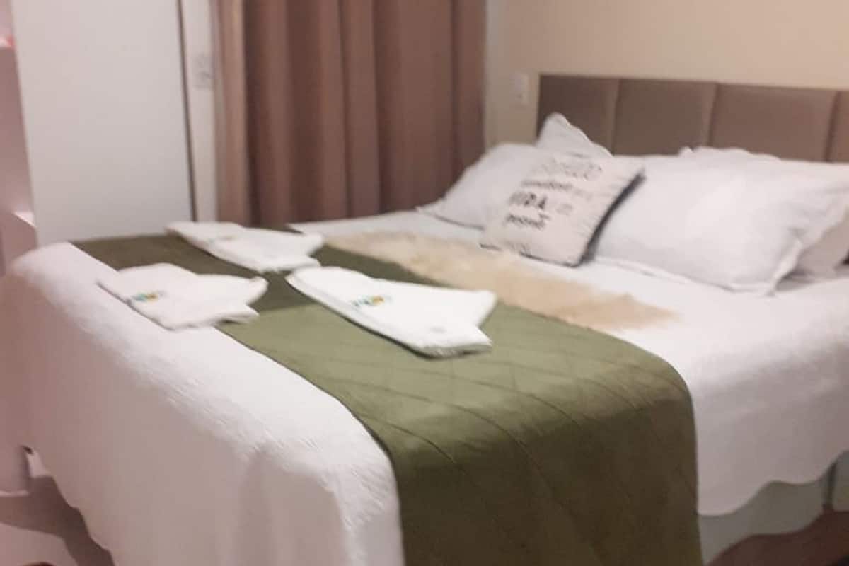 Uma cama bem arrumada com lençóis brancos e um cobertor verde, um travesseiro branco com texto e uma toalha branca ao lado.
