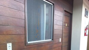 Un mur extérieur en bois, doté d’une grande fenêtre, d’une porte et d’un extincteur fixé au mur.
