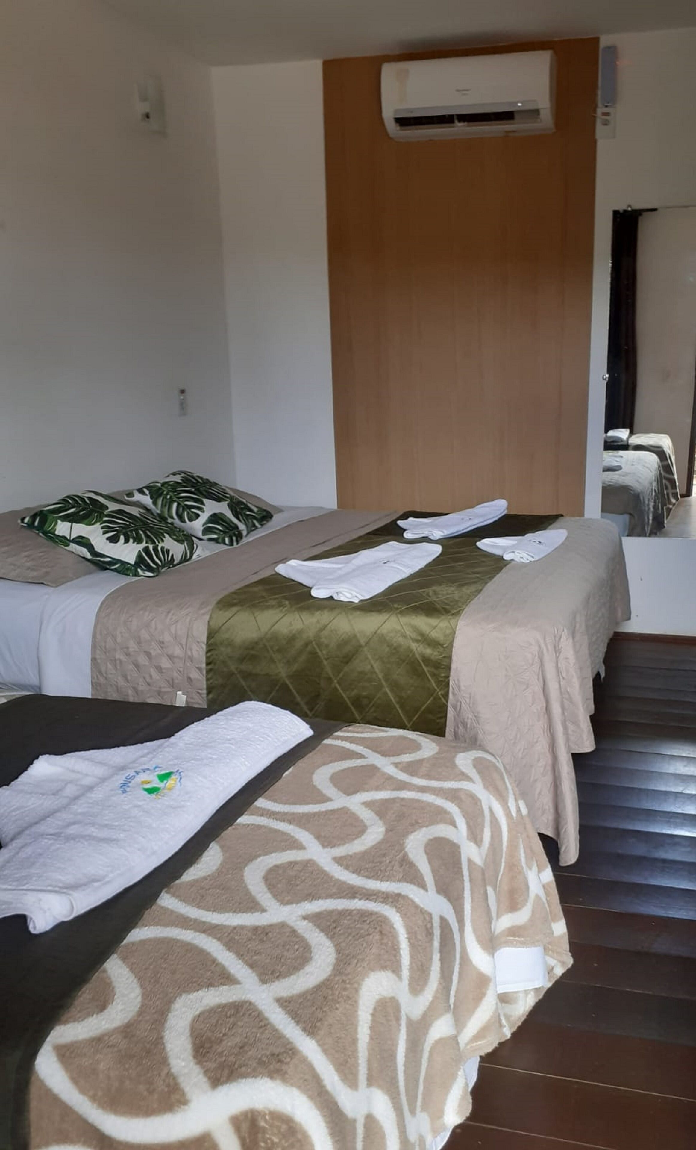 A hotel room with two beds, each with a different patterned bedspread, a wooden headboard, and an air conditioning unit above the beds.