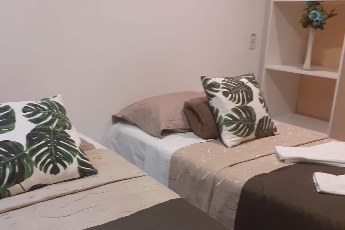 Quarto com duas camas, cada uma com almofada de padrão diferente e uma toalha branca sobre a cama.