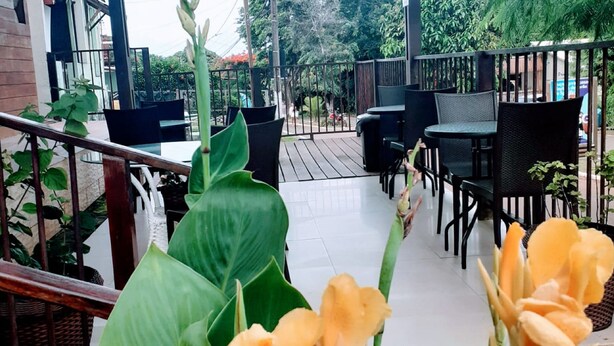 Un espace extérieur aménagé avec des tables et des chaises, entouré de grandes plantes vertes et de fleurs.