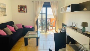 Un salon moderne comprenant un canapé, une table basse et un coin repas. De grandes fenêtres offrent une vue sur l’extérieur.