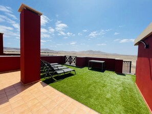 Terraço no telhado com grama sintética, uma mesa e cadeiras de descanso.