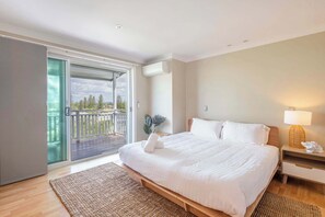 A bedroom with a bed, a nightstand, a lamp, a window, and a balcony.