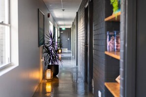 Een gang met een potplant, een wandlamp en een deur met een poster.