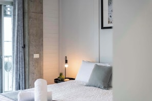 Un dormitorio con cama, una mesita de noche con lámpara, una ventana con cortinas y un cuadro colgado en la pared.