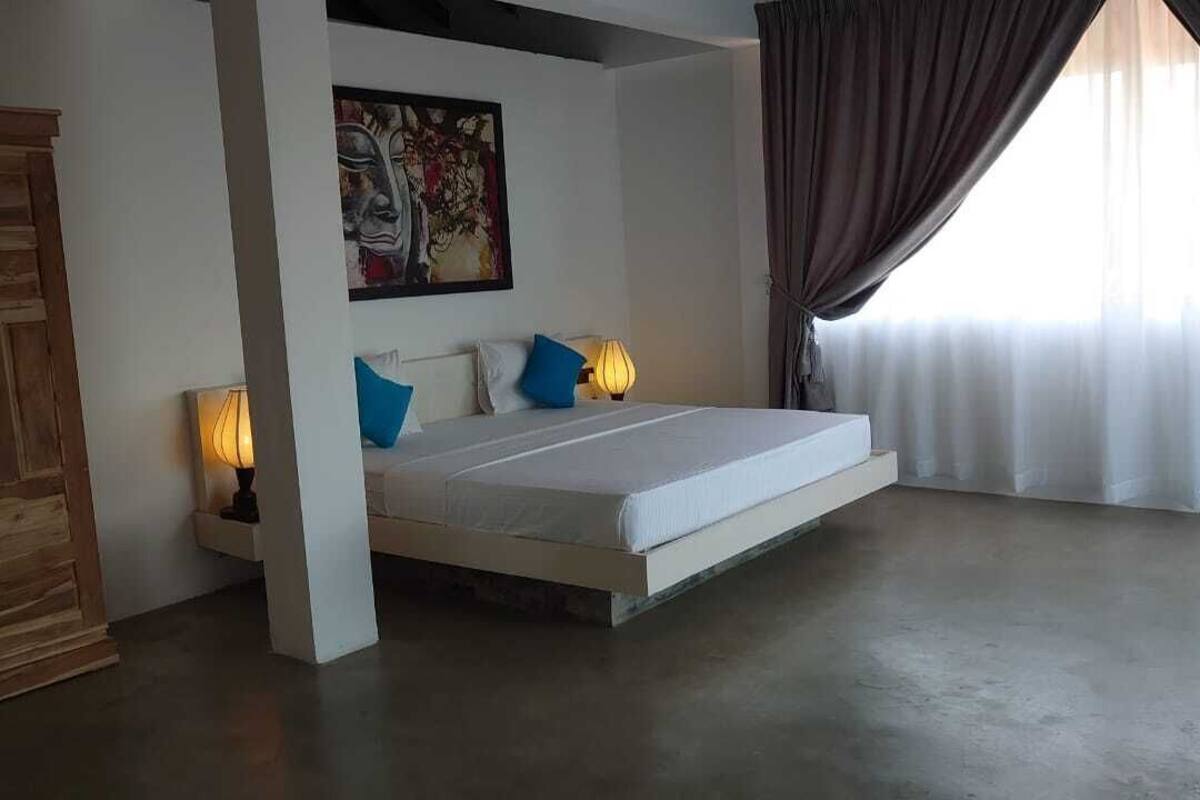 A bedroom with a bed, two bedside lamps, a painting on the wall, and a window with curtains.