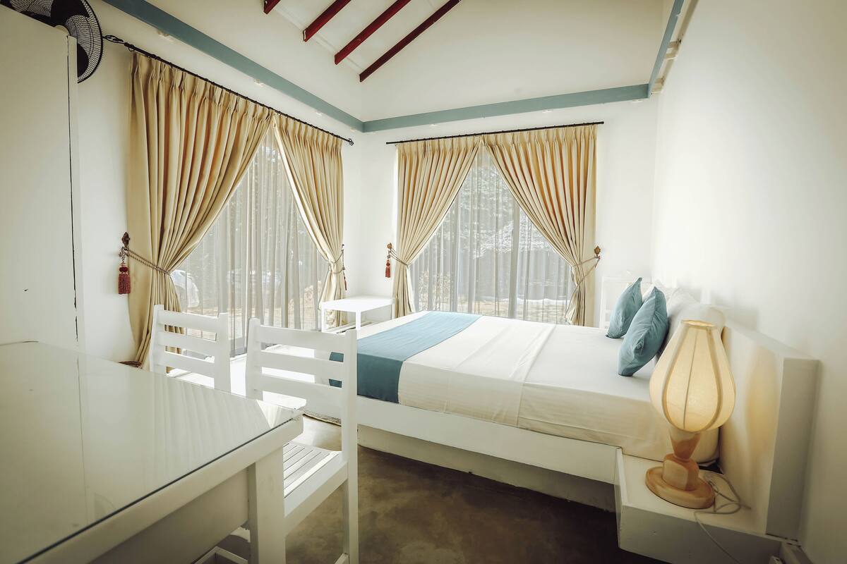 A bedroom with a bed, bedside table, lamp, and a small table with chairs.