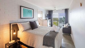 A modern hotel room with a bed, a nightstand, a framed artwork, a balcony with a view, and a ceiling fan. - Yamba Views Room 11 (Yamba)