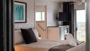A hotel room with a bed, a TV, a painting, and a balcony view. - Yamba Views Room 11 (Yamba)
