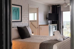 A hotel room with a bed, a TV, a painting, and a balcony view. - Yamba Views Room 11 (Yamba)