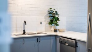 A kitchen with white subway tiles, a black faucet, a dishwasher, and a potted plant. - Yamba Views Apartment (Yamba)