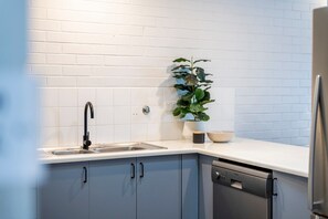 A kitchen with white subway tiles, a black faucet, a dishwasher, and a potted plant. - Yamba Views Apartment (Yamba)