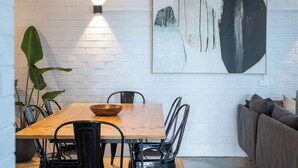 A dining area with a wooden table, black chairs, a black pendant light, a large abstract painting, and a grey sofa. - Yamba Views Apartment (Yamba)