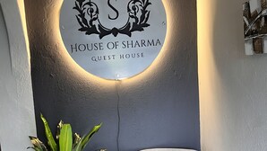 Een bord met een cirkelvormig ontwerp en de tekst 'HOUSE OF SHARMA GUEST HOUSE' voor een gestructureerde muur.
