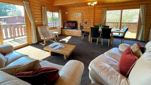 Interior acolhedor de uma cabana de madeira, com sala de estar, mesa de jantar e televisão exibindo 'NETFLIX'.