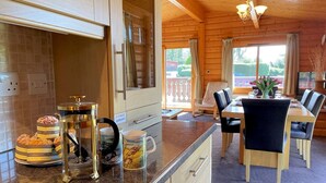 Interior de uma cabana de madeira, com cozinha, bancada de granito, mesa de jantar com cadeiras e varanda com vista.