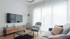 Ein modernes Wohnzimmer mit Flachbildfernseher, Glastisch, Sofa und Sessel.