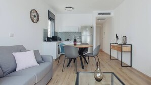 Ein modernes Wohnzimmer mit einem grauen Sofa, einem Glastisch und einem Essbereich mit Stühlen und einem kleinen Tisch.