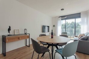 Un salon moderne avec une table de salle à manger ronde en bois, des chaises noires, un canapé gris et un téléviseur fixé au mur.