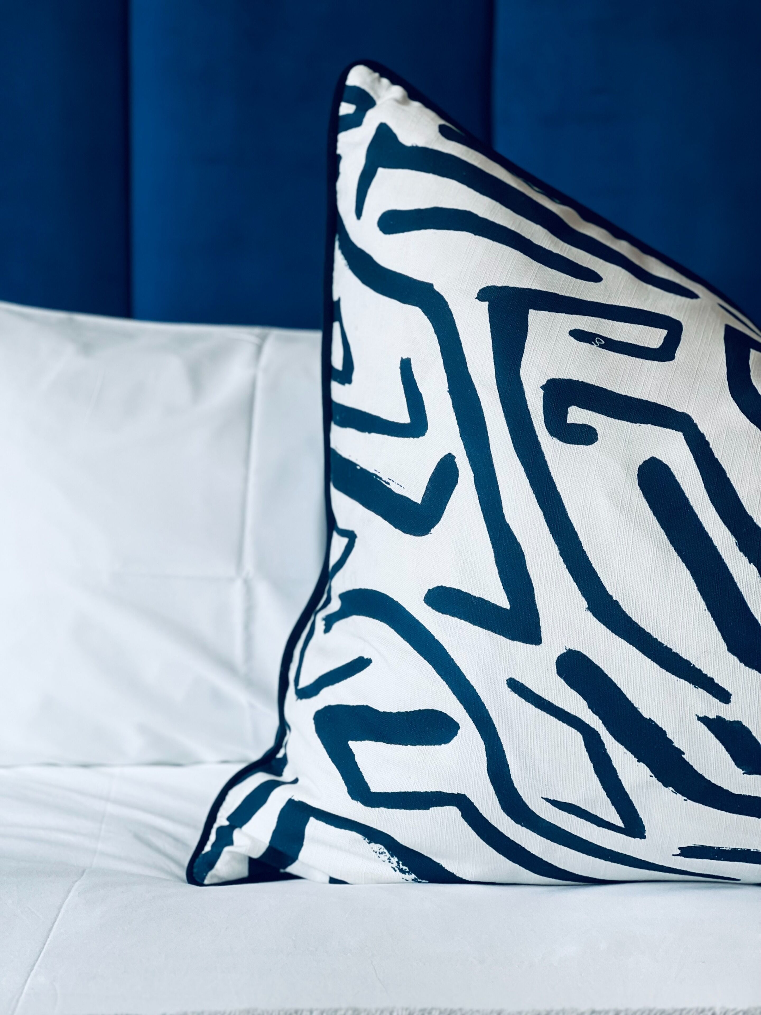 Un almohadón con un estampado geométrico sobre una cama blanca.