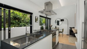 A modern kitchen with a central island, stainless steel appliances, and a large window offering a view of greenery. - Designer Apartment in Sea Point (Cape Town)
