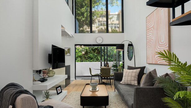 A modern living room with a sofa, coffee table, and a TV. There is a dining area with chairs and a table. The room has large windows and a view of greenery outside. - Designer Apartment in Sea Point (Cape Town)