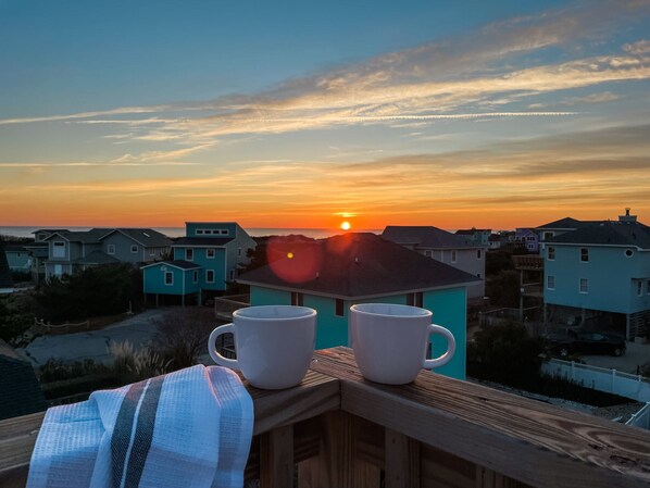 A sunset view from a balcony with two white mugs and a striped cloth.