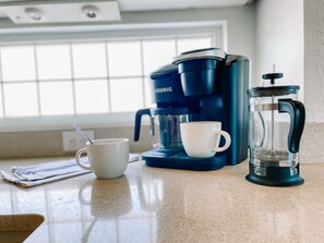 A kitchen counter with a coffee maker, a coffee pot, and a cup.