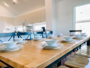 A long wooden table with white bowls and saucers arranged for dining.