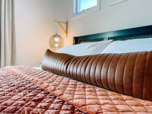 A neatly made bed with a brown leather headboard and a quilted bedspread.