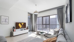 A modern living room with a large window, a sofa, a coffee table, and a TV on a white cabinet. - 
Vogue, Downtown Bellevue Towers near Burj Khalifa and Dubai Mall (دبي)