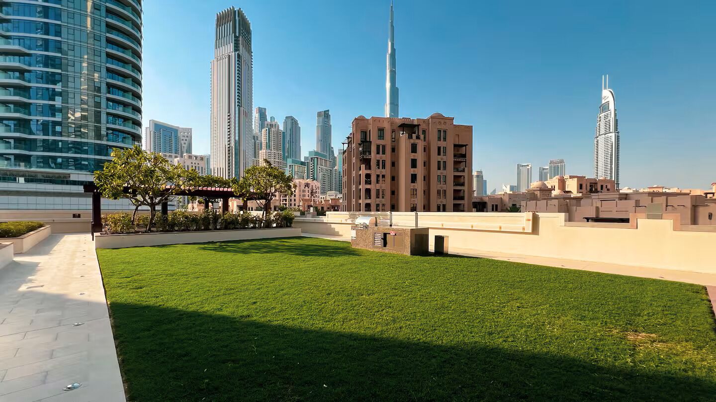 A landscaped area with a pathway, a small garden, and modern buildings in the background.