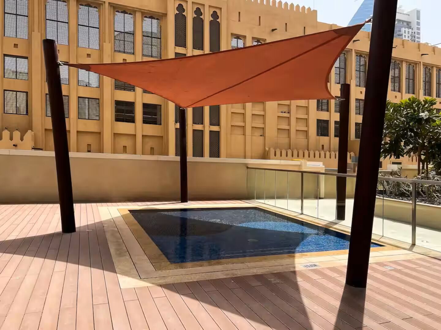 Ein Pool auf dem Dach mit Sonnenschutzbereich, umgeben von einer Holzdar Terrasse und einem Gebäude mit großen Fenstern im Hintergrund.